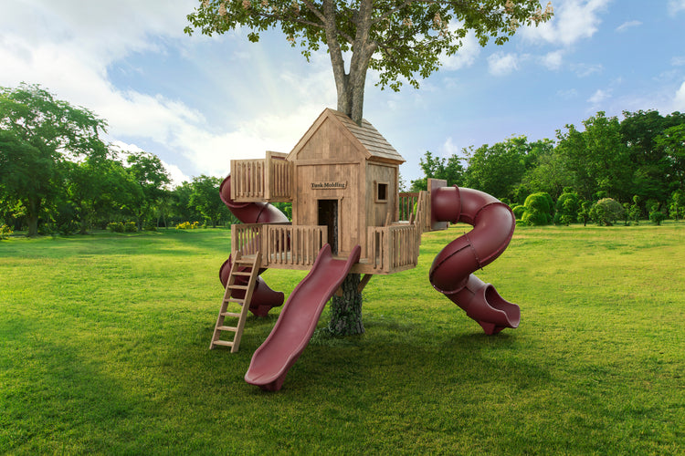 Wooden playhouse with red slides on a grassy area with trees in the background